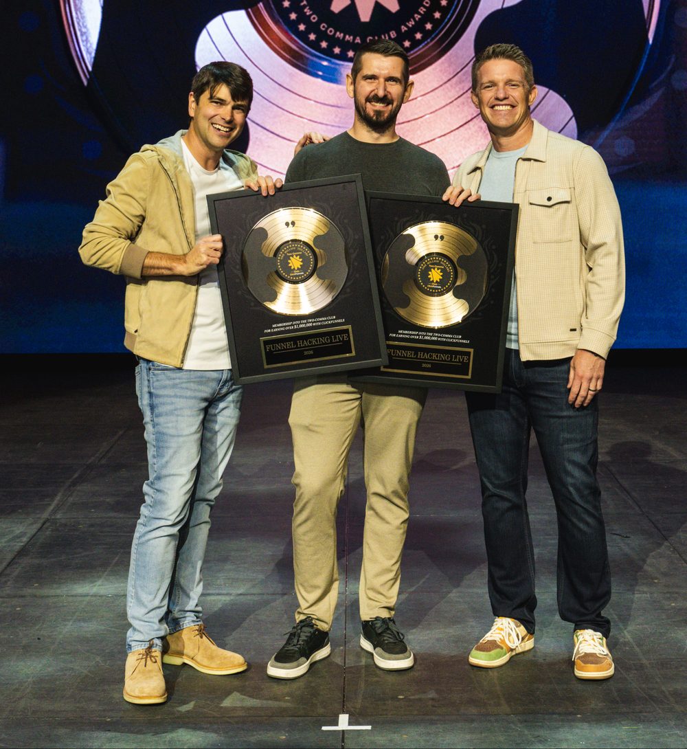 Kenneth Rebech on stage with Russell Brunson, holding two Two Comma Club awards